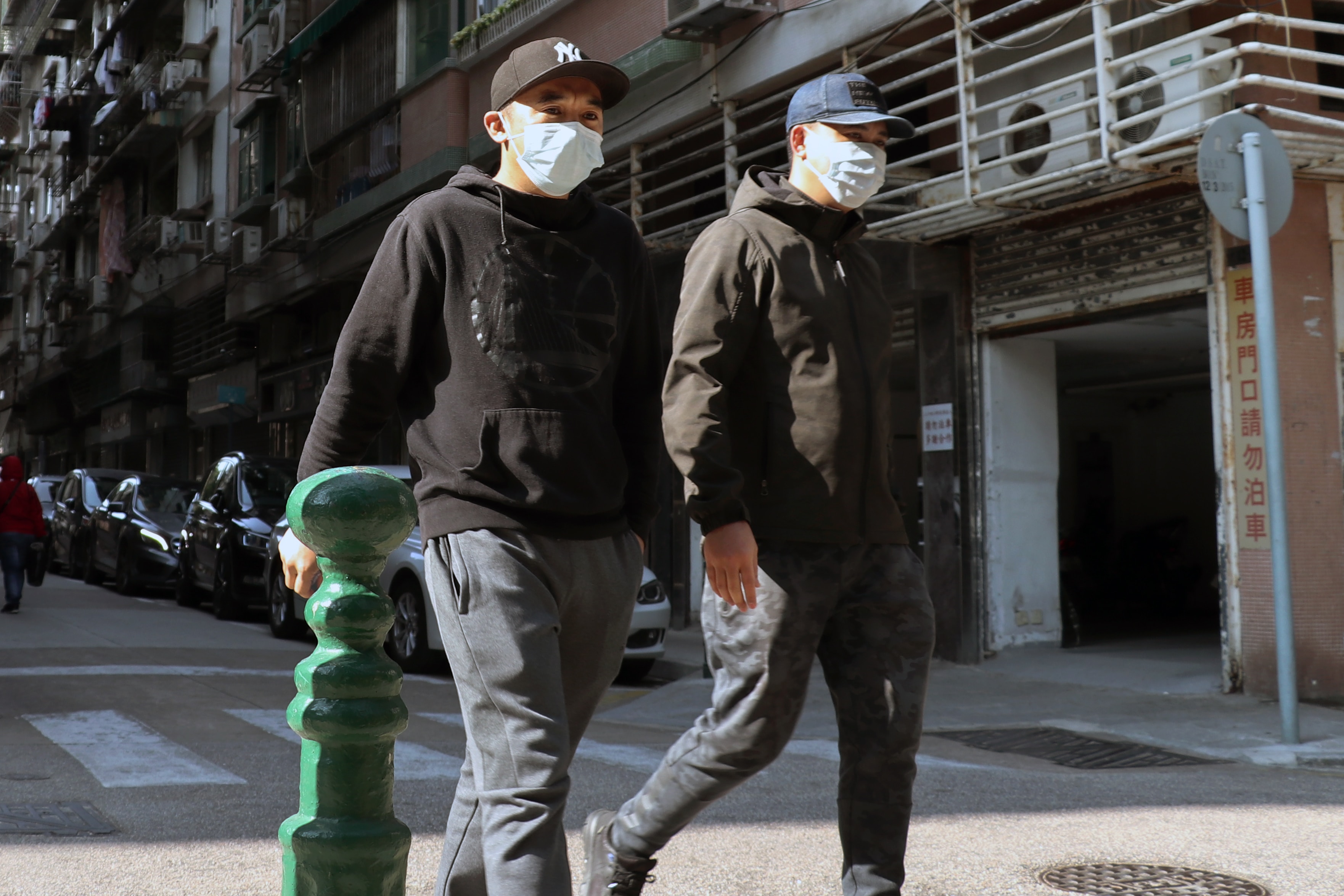 Two men wearing masks while walking down a street