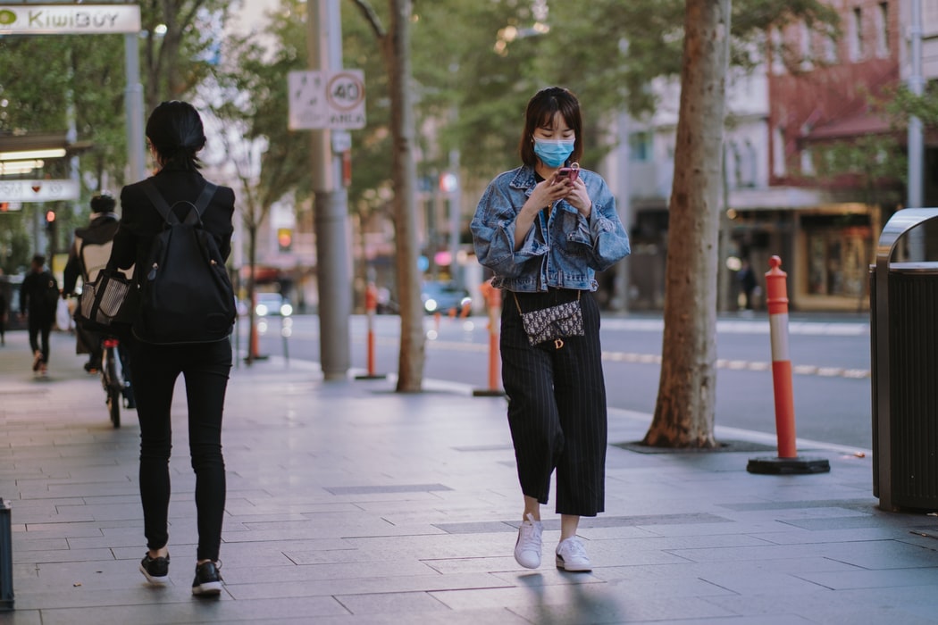 A girl wearing a mask and using her phone while walking down a street