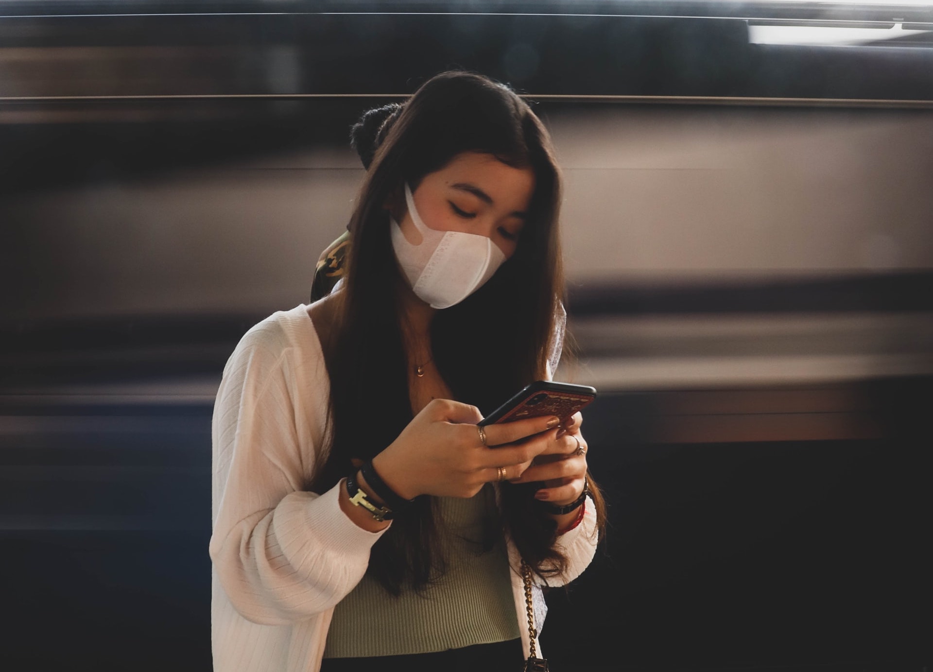 Girl wearing a mask and using her phone at the train station